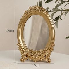 an ornate gold framed mirror sitting on top of a table next to a potted plant