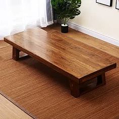 a wooden coffee table sitting on top of a rug next to a potted plant