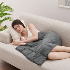 a woman laying on a couch with her eyes closed while she's sleeping under a blanket