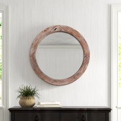 a round wooden mirror hanging on the wall above a dresser with a potted plant