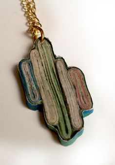 a piece of wood is hanging from a gold chain on a white surface with a black and green design