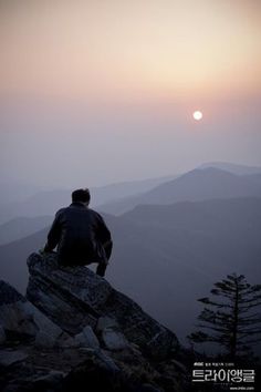 a man sitting on top of a mountain looking at the sun