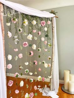 a white curtain with pink and white flowers hanging from it's side next to candles