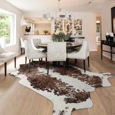 a dining room table with white chairs and brown cow hide rug on the wooden floor