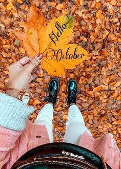 a person holding an autumn leaf with the words hello october written on it in front of them