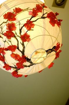 a white lamp with red flowers hanging from it's side and a circular light fixture in the background