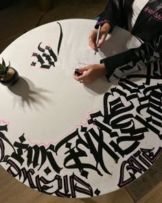 a person writing on a piece of paper that has graffiti all over it, with a plant in the background