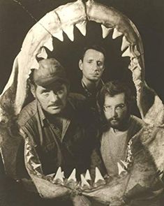 three men are standing in front of a shark's mouth with teeth on it