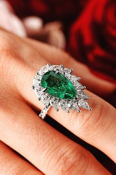 a woman's engagement ring with an emerald and diamond halo setting on her finger