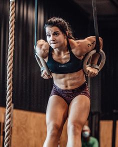 a woman in a black bra top and purple shorts is hanging on a rope with two hands