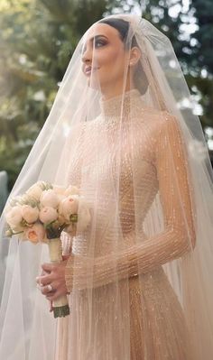 a woman in a wedding dress holding a bouquet and wearing a veil over her head