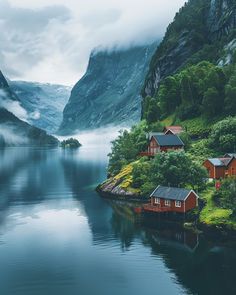 some houses on the shore of a lake with mountains in the backgrouds