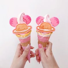 two hands holding ice cream cones with pink frosting and ears shaped like mouse heads