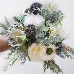 a bouquet of white flowers and greenery in someone's hand on a white background