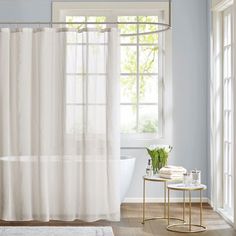 a white bath tub sitting under a window next to a table with flowers on it