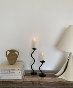 two black candles are next to each other on a table with books and a vase