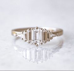 a three stone diamond ring sitting on top of a white surface with reflection in the middle