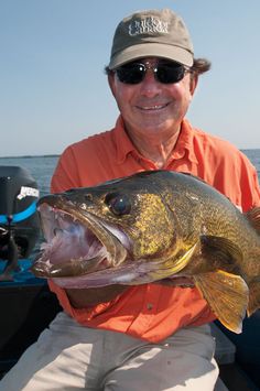 a man in an orange shirt is holding a large fish while sitting on a boat