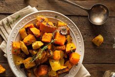 a white plate topped with roasted potatoes on top of a wooden table next to silverware