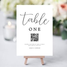 a table sign sitting on top of a wooden easel with flowers in the background