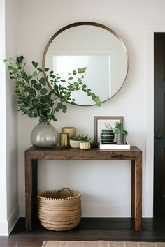 a wooden table topped with a mirror and potted plant next to a vase filled with greenery