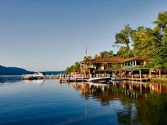 a lake with boats and houses on the shore in front of it, surrounded by trees