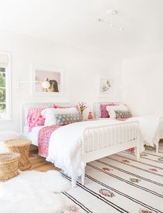 a white bedroom with pink and blue bedding, rugs and pictures on the wall