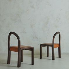 two chairs sitting next to each other in front of a white wall and cement floor