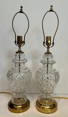 two clear glass lamps sitting on top of a white table next to each other with gold trimmings