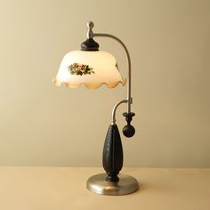 a table lamp with a flowered glass shade on it's arm and base