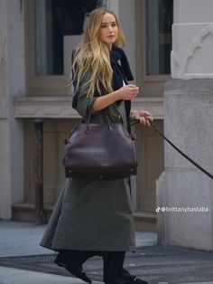 a woman walking her dog down the street with a purse on it's leash