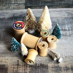 several wooden spools with christmas trees in them on a wood floor, one is empty and the other has some tinsel