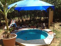 an above ground pool with a blue umbrella and some chairs in the backround