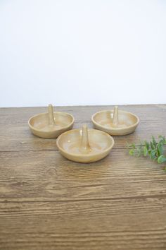 three small bowls on a wooden table with plants in the middle and one is empty