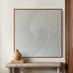 a vase sitting on top of a wooden table next to a wall mounted art piece