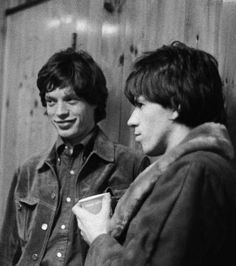 two young men standing next to each other in front of a wooden wall and talking