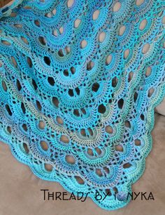 a blue crocheted shawl with holes in the middle on a couch next to pillows