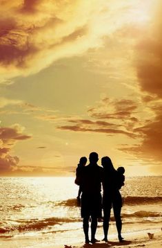 three people are standing on the beach with their arms around each other as the sun sets