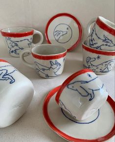 a table topped with cups and saucers covered in blue and red hand painted animals