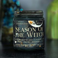 a jar of season of the witch candle sits on a table next to a potted plant