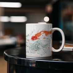 a white coffee mug with a goldfish on it sitting on a black round table