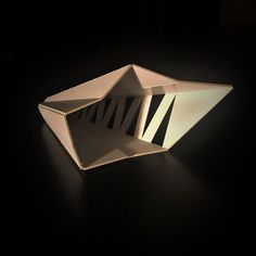 an origami bowl sitting on top of a black table with light coming from it