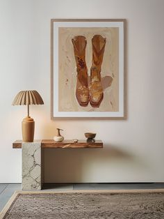 a painting hanging on the wall next to a table with a lamp and vase in it