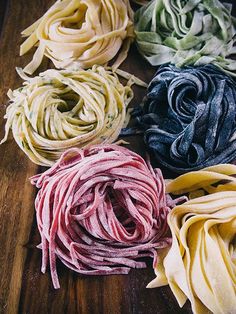 four different colors of pasta on a wooden table