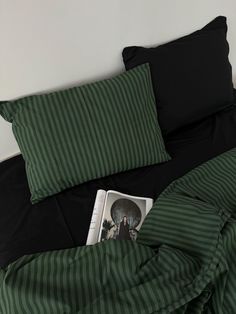 a bed with black and green sheets, pillows and a magazine laying on top of it