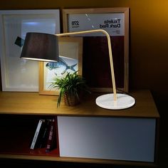 a desk lamp sitting on top of a wooden table next to a book shelf and framed pictures