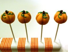 four pumpkin shaped cake pops sitting on top of a white tablecloth covered stand with orange checkered ribbon