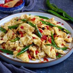 a white plate topped with eggs and green beans next to a bowl filled with peppers