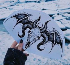 a hand holding up a sticker with an image of a dragon on it in the snow