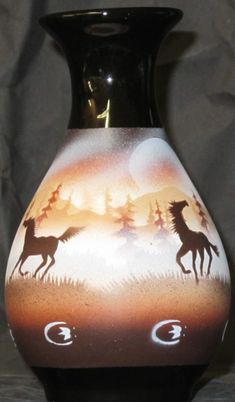 a black vase with horses painted on it's sides and trees in the background